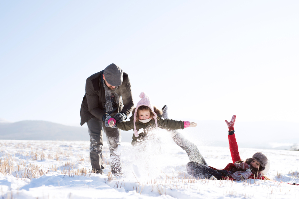 Father and mother having fun with their daughter, playing in the snow. Sunny white winter nature.