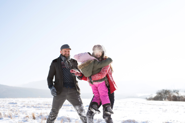 Father and mother outside having fun with their daughter, playing in the snow. Sunny white winter nature.