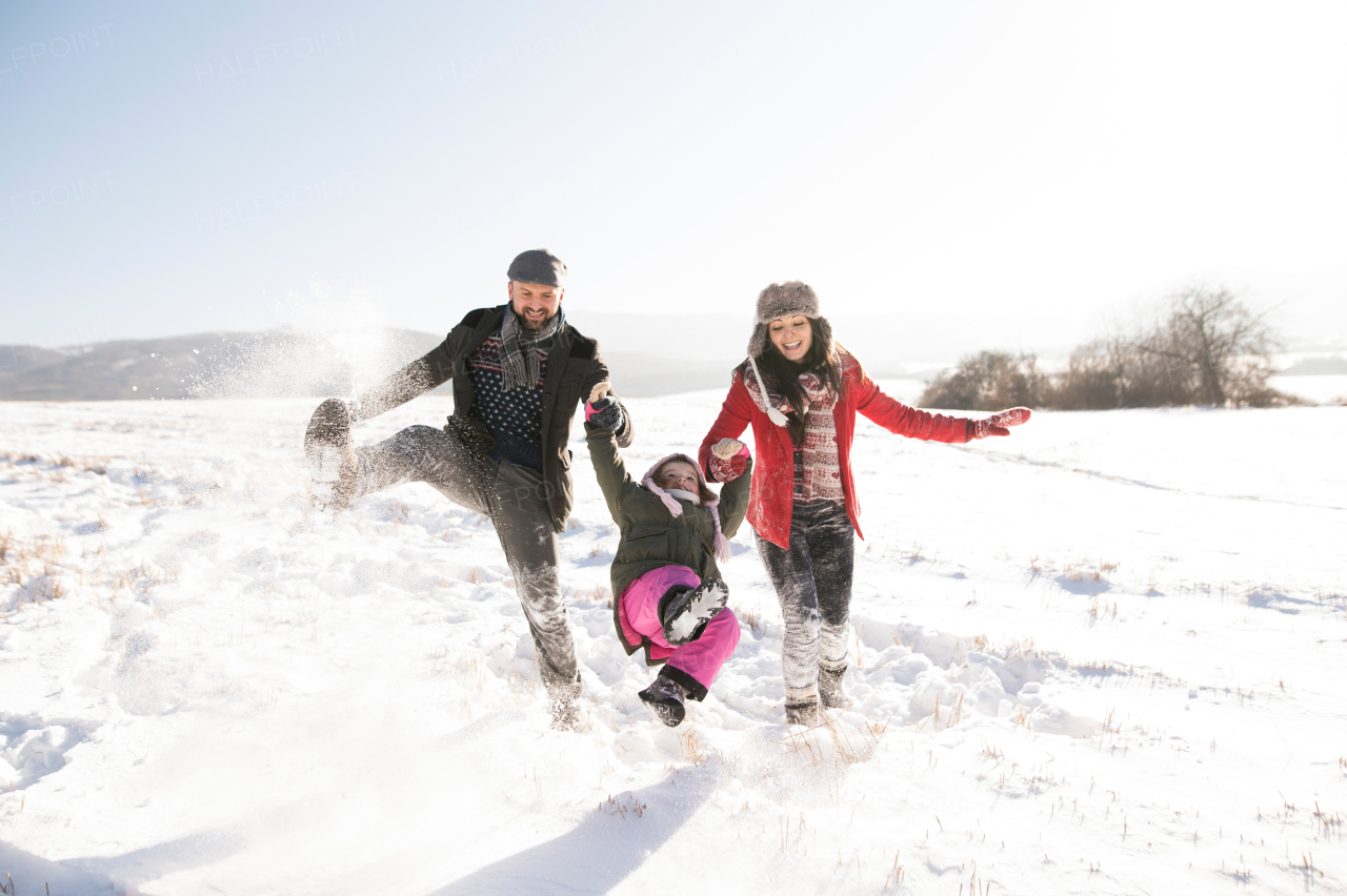 Father and mother having fun with their daughter, playing in the snow. Sunny white winter nature.