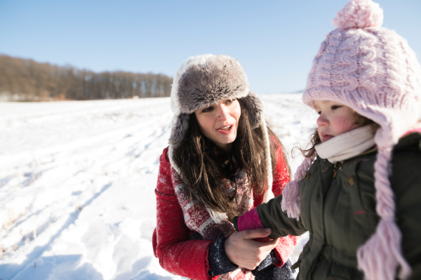 Young mother having fun with her daughter, playing in the snow. Sunny white winter nature.