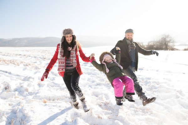 Father and mother having fun with their daughter, playing in the snow. Sunny white winter nature.