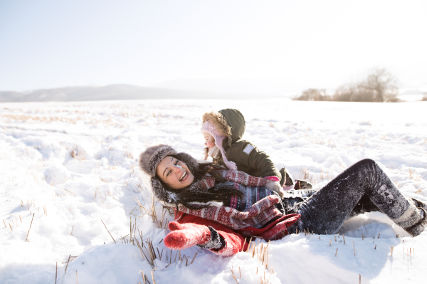 Young mother having fun with her daughter, playing in the snow. Sunny white winter nature.