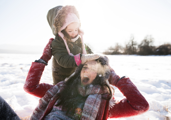 Young mother having fun with her daughter, playing in the snow. Sunny white winter nature.