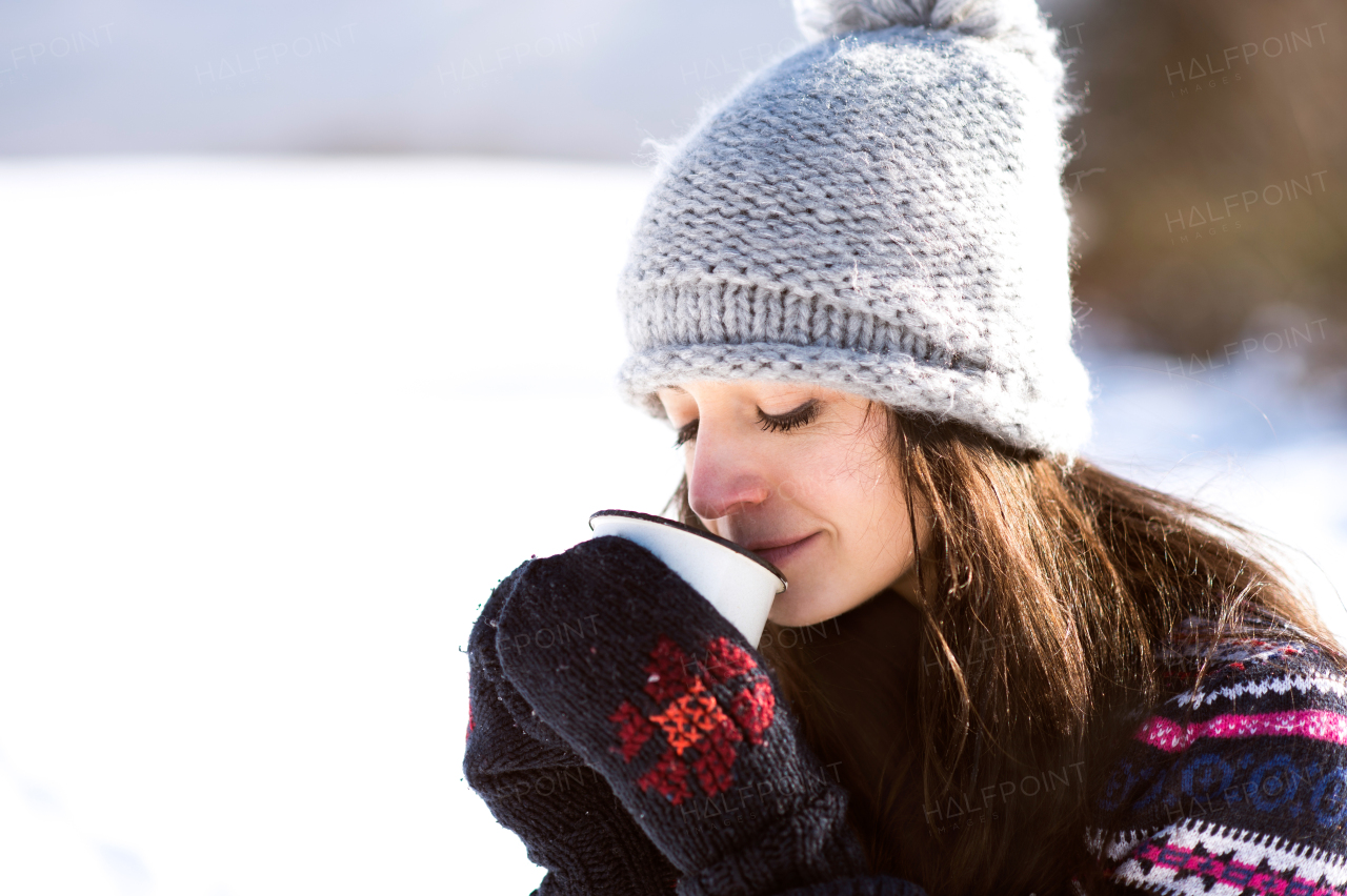 Beautiful young woman in knitted hat and gloves holding a cup of coffee outside in winter nature