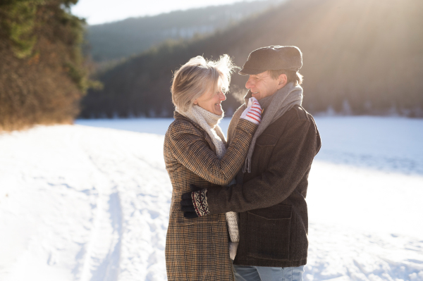 Beautiful senior woman and man on a walk in sunny winter nature hugging.