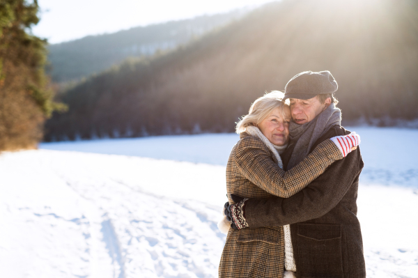 Beautiful senior woman and man on a walk in sunny winter nature hugging.