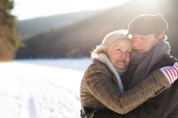 Beautiful senior woman and man on a walk in sunny winter nature hugging.