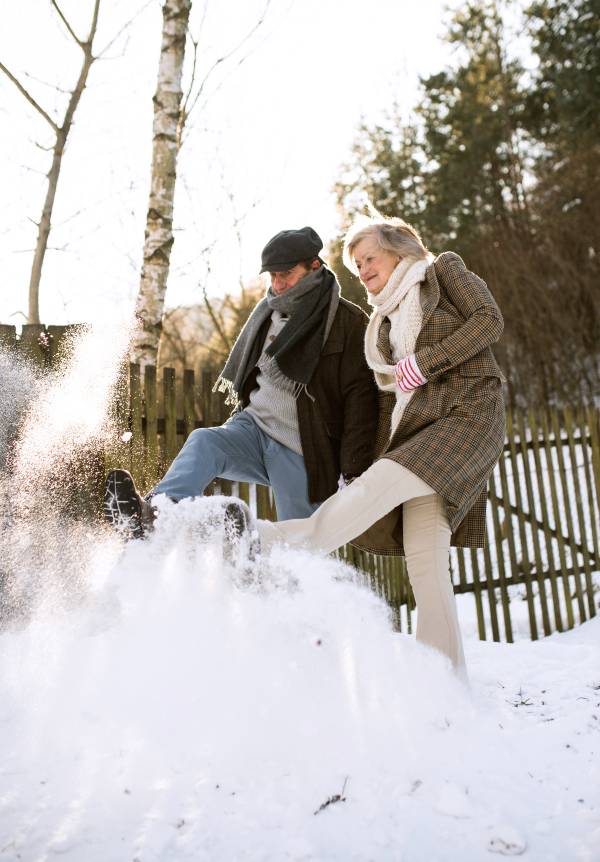 Beautiful senior woman and man on a walk in sunny winter nature, kicking snow.