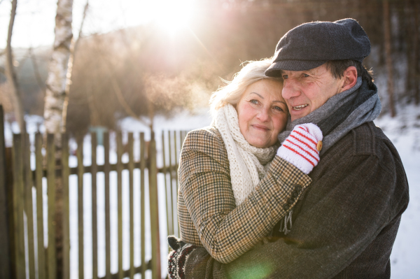 Beautiful senior woman and man on a walk in sunny winter nature, hugging