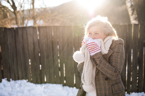 Beautiful senior woman on a walk in sunny winter nature, standing against wooden fence.