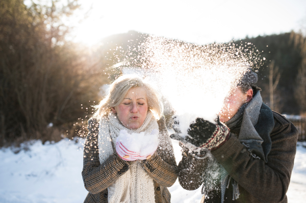 Beautiful senior woman and man on a walk in sunny winter nature, blowing snow.