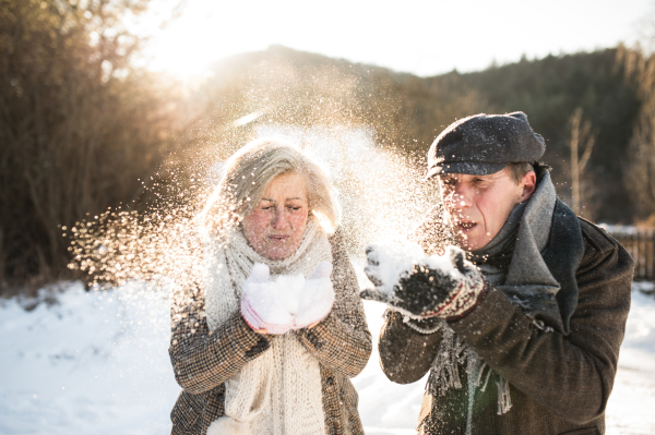 Beautiful senior woman and man on a walk in sunny winter nature, blowing snow.