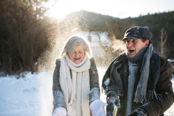 Beautiful senior woman and man on a walk in sunny winter nature, blowing snow.