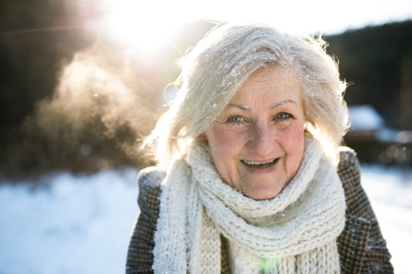 Beautiful senior woman on a walk in sunny winter nature, covered by snow.