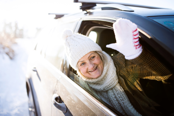 Beautiful senior woman in winter clothes in a car, waving