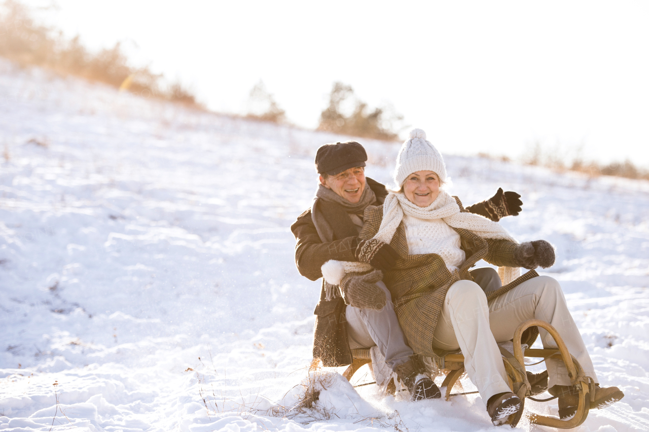 Beautiful senior woman and man on sledge having fun in sunny winter nature.