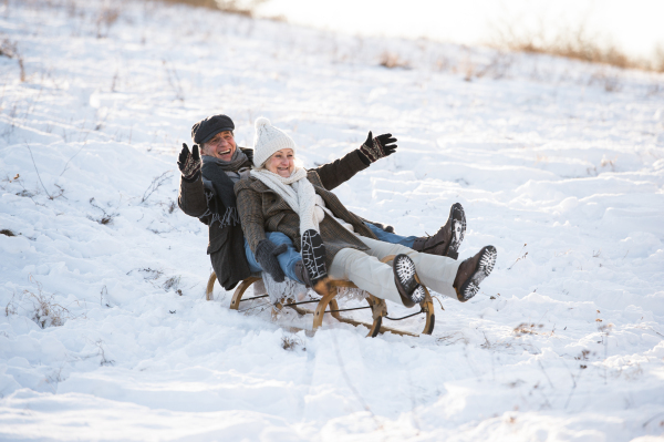 Beautiful senior woman and man on sledge having fun in sunny winter nature.