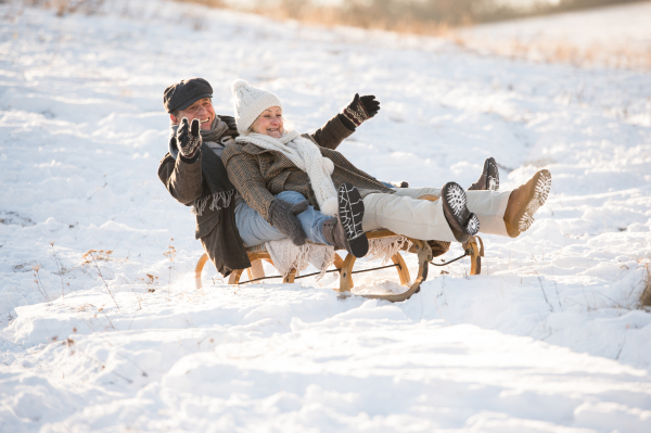 Beautiful senior woman and man on sledge having fun in sunny winter nature.