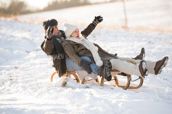 Beautiful senior woman and man on sledge having fun in sunny winter nature.