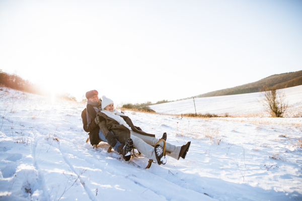 Beautiful senior woman and man on sledge having fun in sunny winter nature.