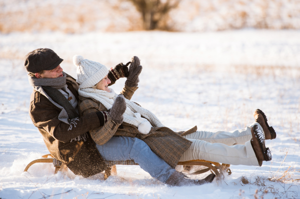 Beautiful senior woman and man on sledge having fun in sunny winter nature.