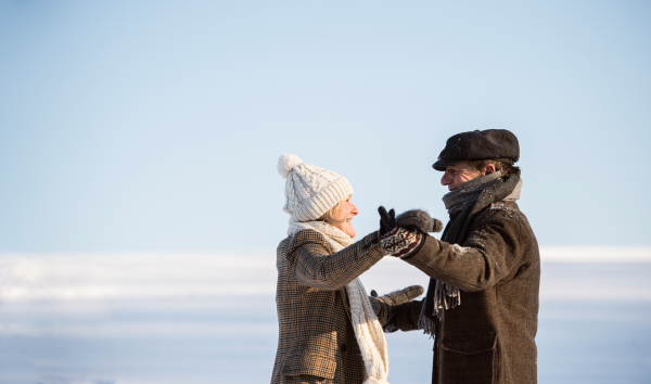 Beautiful senior woman and man on a walk in sunny winter nature, holding hands and looking at each other.