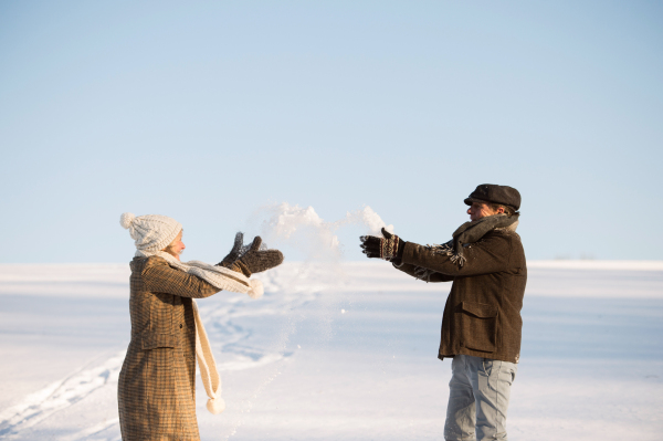 Beautiful senior woman and man on a walk in sunny winter nature, enjoying snow and having fun.