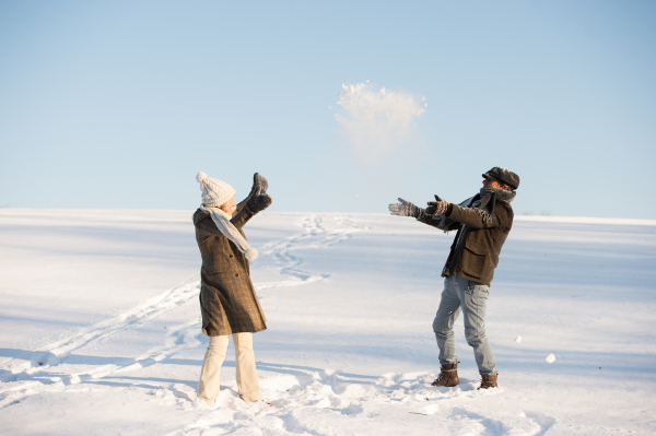 Beautiful senior woman and man on a walk in sunny winter nature, enjoying snow and having fun.