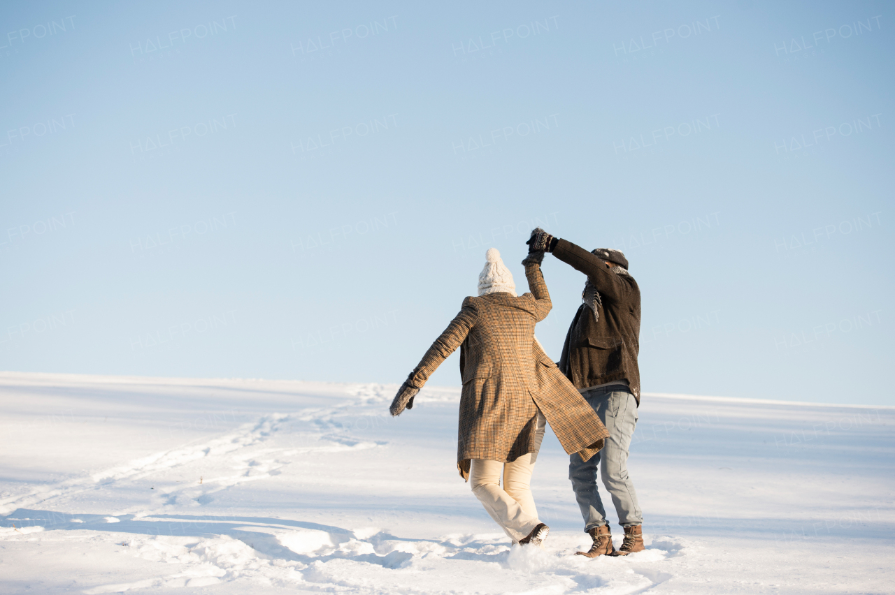 Beautiful senior woman and man on a walk in sunny winter nature, holding hands and dancing.