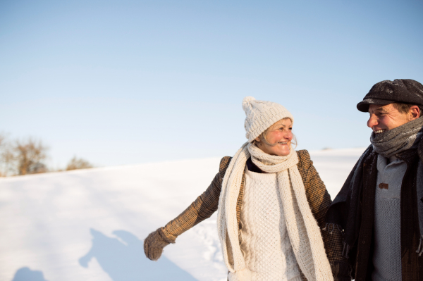 Beautiful senior woman and man on a walk in sunny winter nature, enjoying snow and having fun.