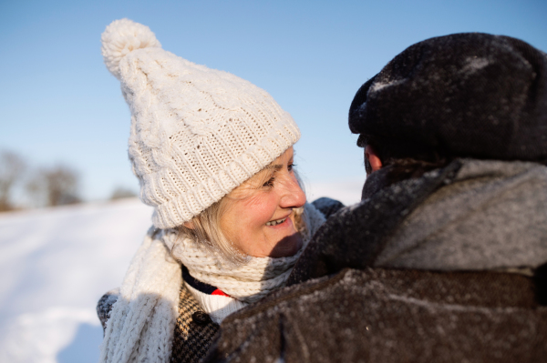 Beautiful senior woman and man on a walk in sunny winter nature, enjoying snow and having fun.