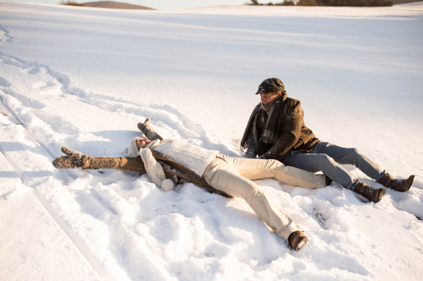 Beautiful senior woman and man on a walk in sunny winter nature, enjoying snow and having fun.