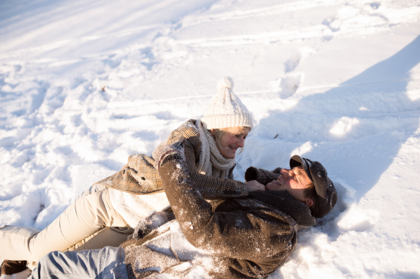 Beautiful senior woman and man on a walk in sunny winter nature, enjoying snow and having fun.