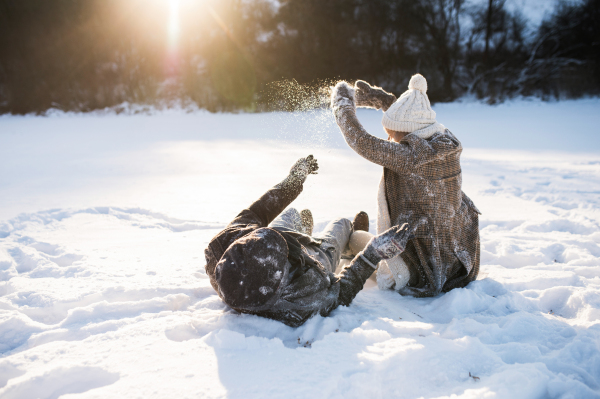 Beautiful senior woman and man on a walk in sunny winter nature, enjoying snow and having fun.