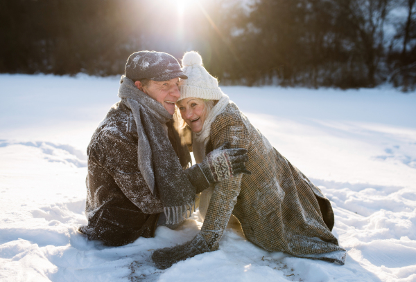 Beautiful senior woman and man on a walk in sunny winter nature, enjoying snow and having fun.