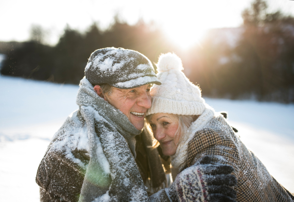 Beautiful senior woman and man on a walk in sunny winter nature, enjoying snow and having fun.