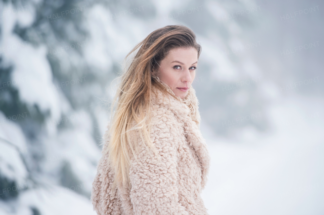 Beautiful young blonde woman in fur coat on a walk in winter nature. Snowy day.