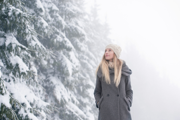 Beautiful young blonde woman in gray coat on a walk in winter nature. Snowy day.