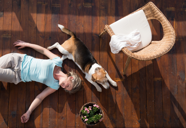 Beautiful senior woman with her dog at home, lying on wooden terrace, relaxing