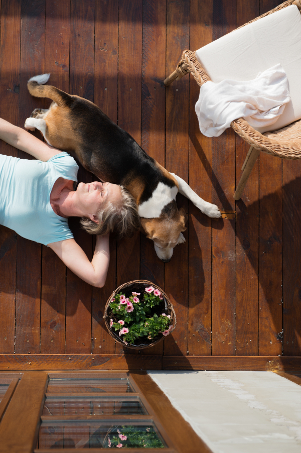 Beautiful senior woman with her dog at home, lying on wooden terrace, relaxing