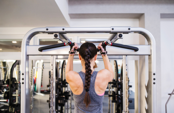 Close up of attractive fit woman flexing back muscles on cable machine, back view, rear viewpoint