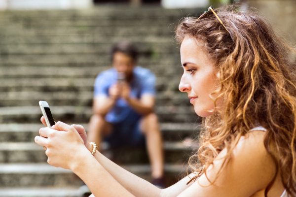 Beautiful young couple with smart phones sitting on stairs in town, texting. Sunny spring day.