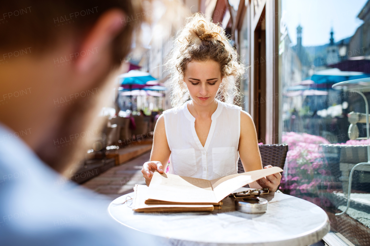 Beautiful young woman with her boyfriend sitting in cafe, reading something. Sunny spring day.