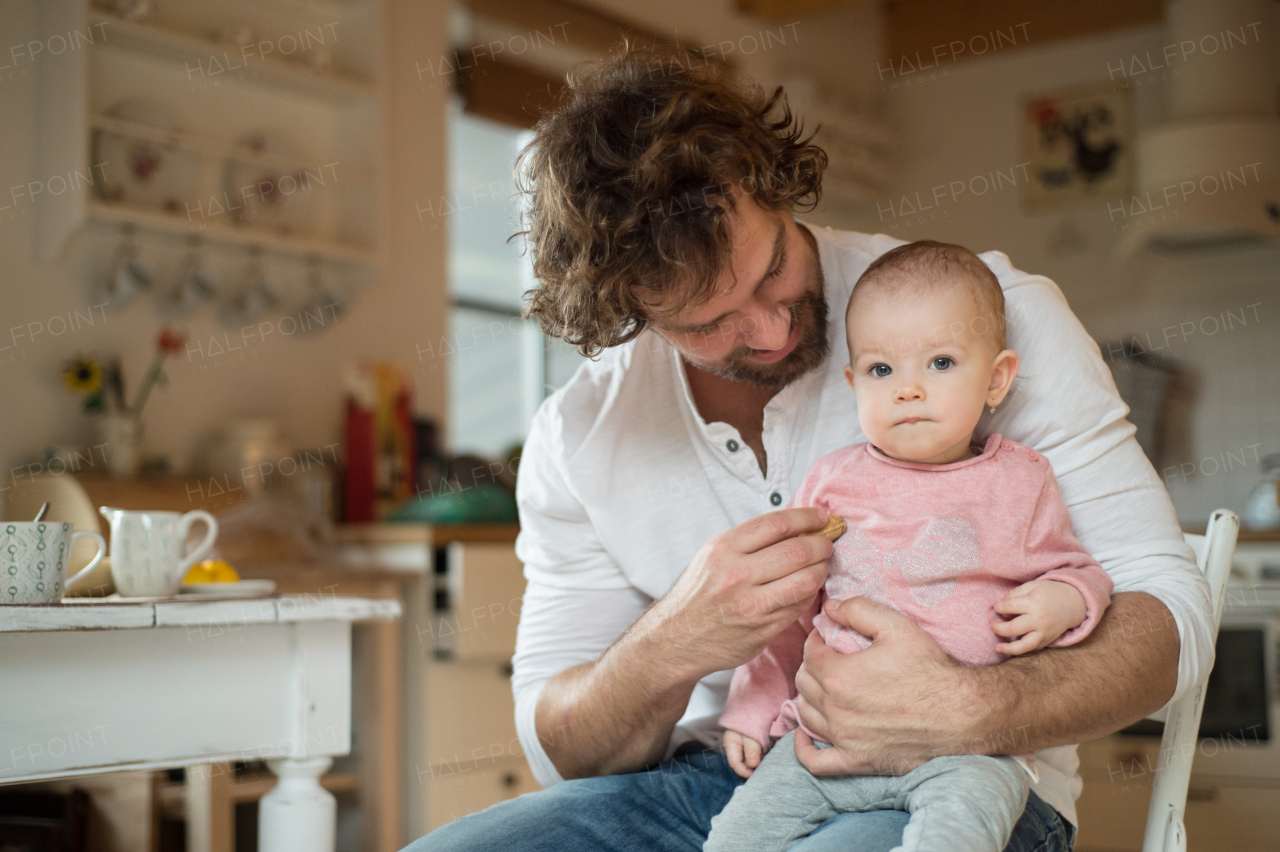 Young father at home holding his cute little daughter in his lap