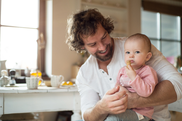 Young father at home holding his cute little daughter in his lap