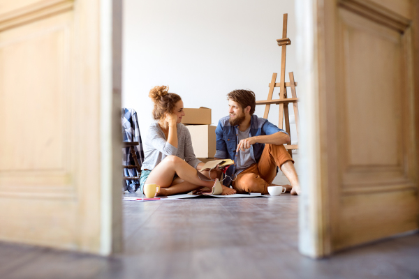 Young married couple moving in new house, sitting on the floor near cardboard boxes, sitting and resting.