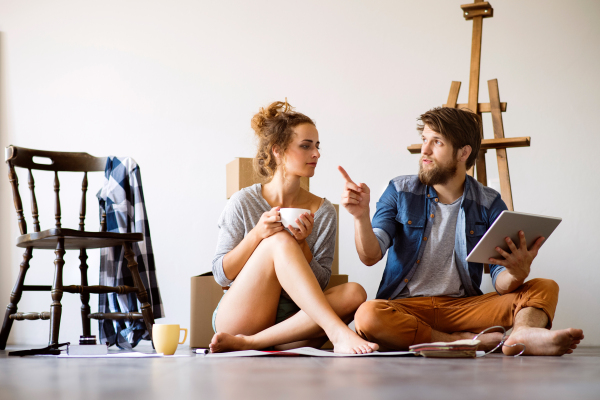 Young married couple with tablet moving in a new house, resting and making plans.