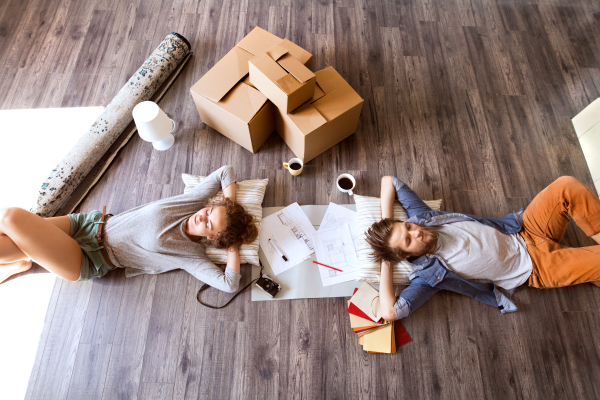 Young married couple moving in new house, lying on the floor near cardboard boxes, drinking coffee.