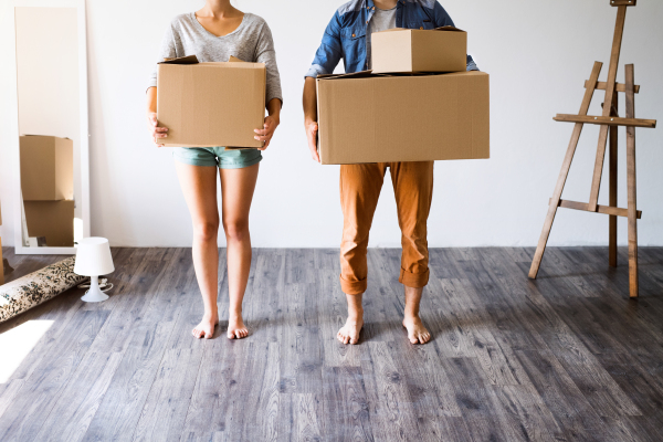 Unrecognizable young married couple moving in new house, holding big cardboard boxes.