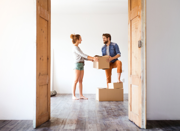 Young married couple moving in new house, holding big cardboard boxes.